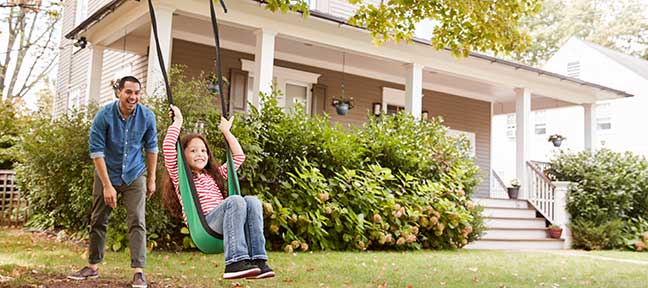 father pushing daughter on swing in front yard